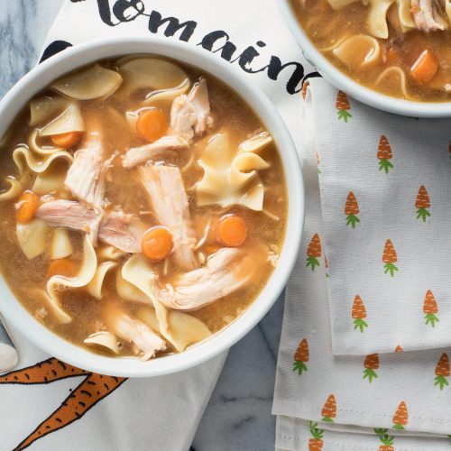 Turkey noodle soup with carrots in a white bowl.