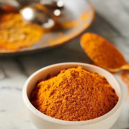 Bowl of Indian restaurant spice mix with spice dusted plate behind it from the front.