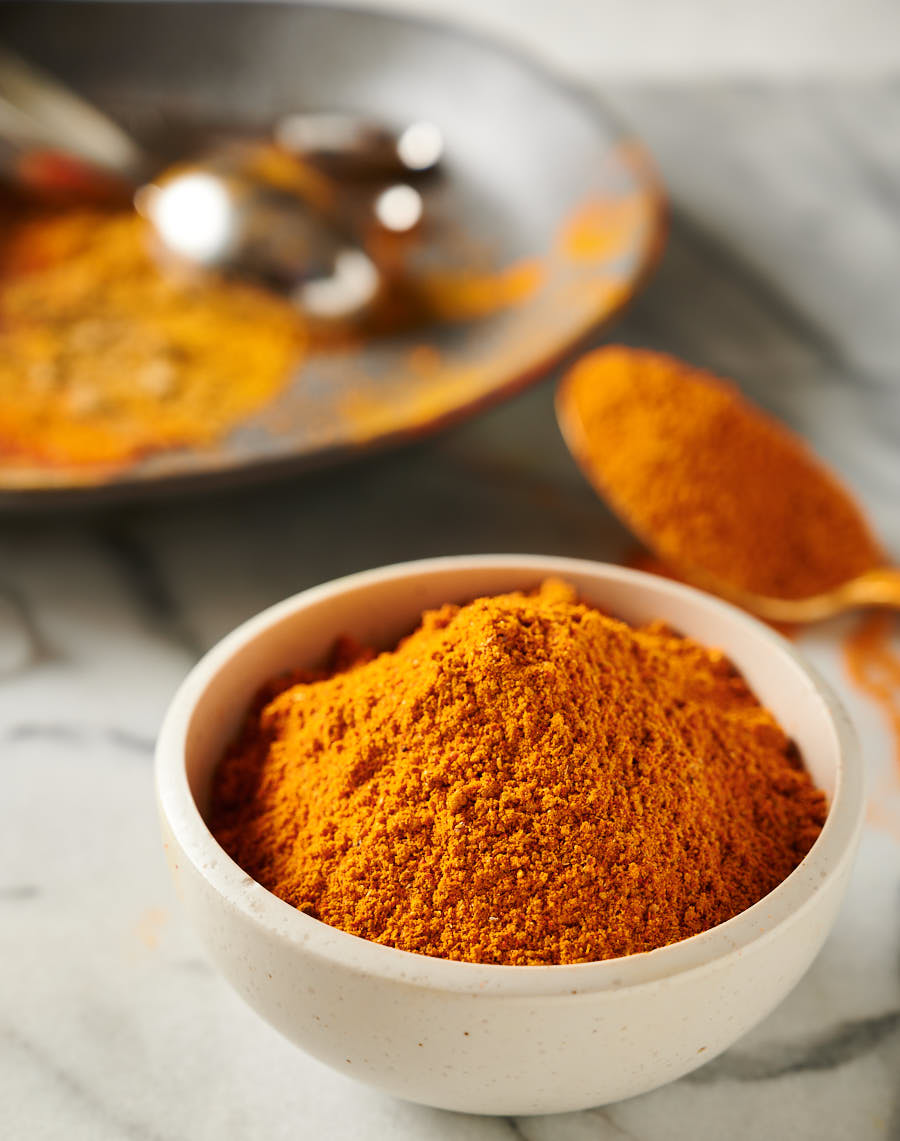 Bowl of Indian restaurant spice mix with spice dusted plate behind it from the front.