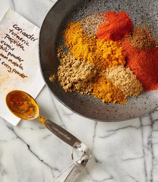 Individual spices on a plate with recipe card and measuring spoons.