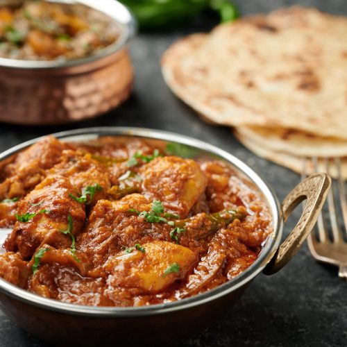 Dopiaza curry in an Indian copper bowl with parathas.