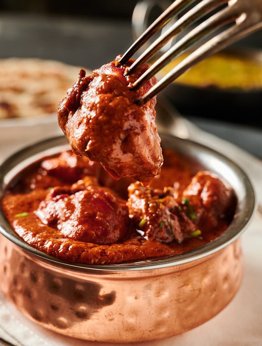 Piece of chicken tikka masala on a fork.