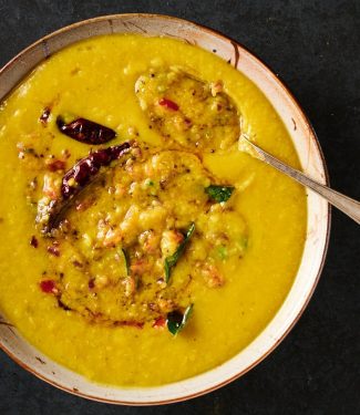 Mixing bowl of tarka dal with tarka mixed in partially from above.