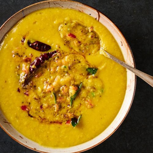 Mixing bowl of tarka dal with tarka mixed in partially from above.