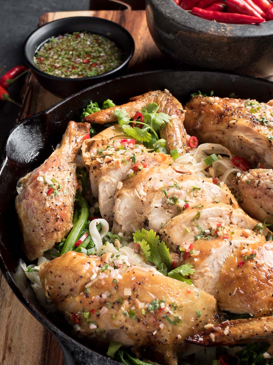 Thai roast chicken on a bed of rice noodles in a black cast iron skillet.