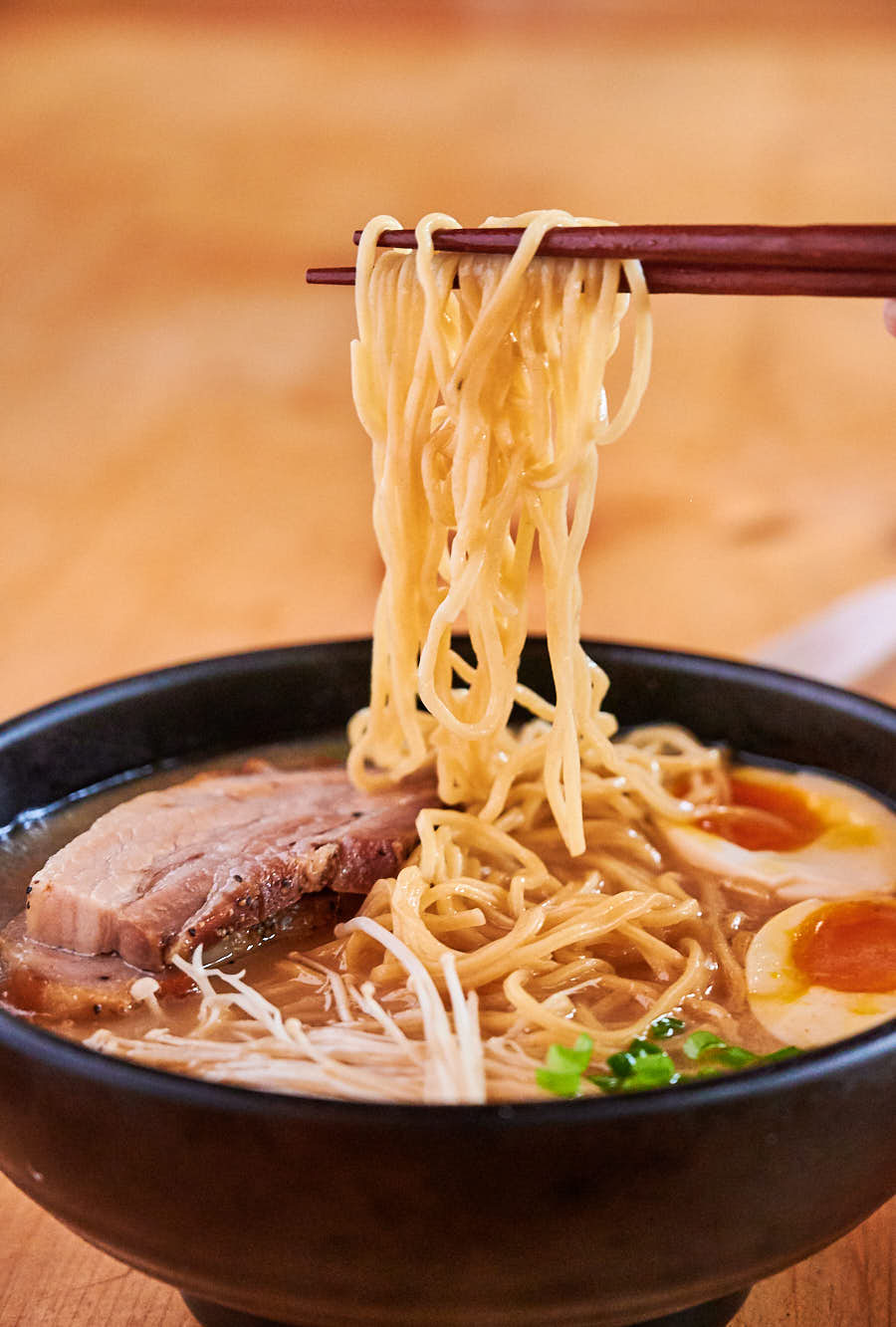 Chopsticks holding a big scoopful of noodles above the bowl.