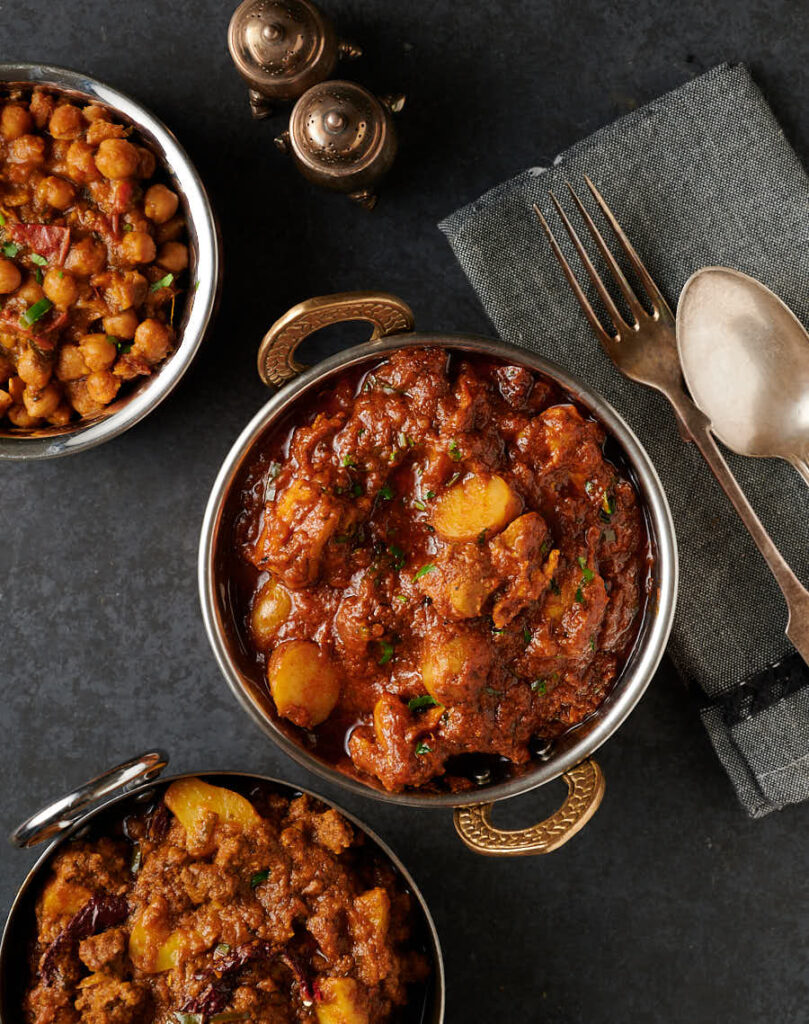 Dinner table scene with aloo chicken curry in an brass handled bowl.