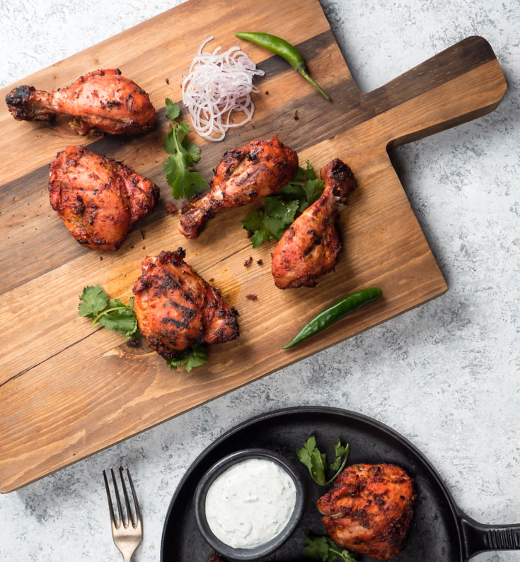 Tandoori chicken on a board with green chilies.