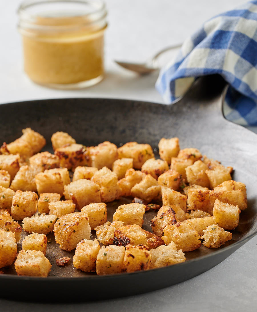 Golden, buttery croutons in a dark skillet from the front.