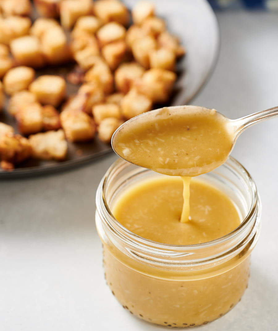 Spoon drizzling Caesar salad dressing into mason jar.