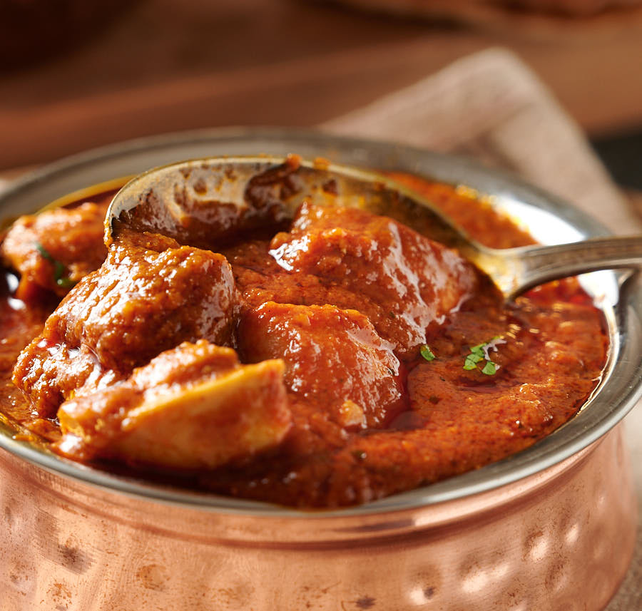 Bowl of restaurant style pathia curry with a spoon in it from the front.