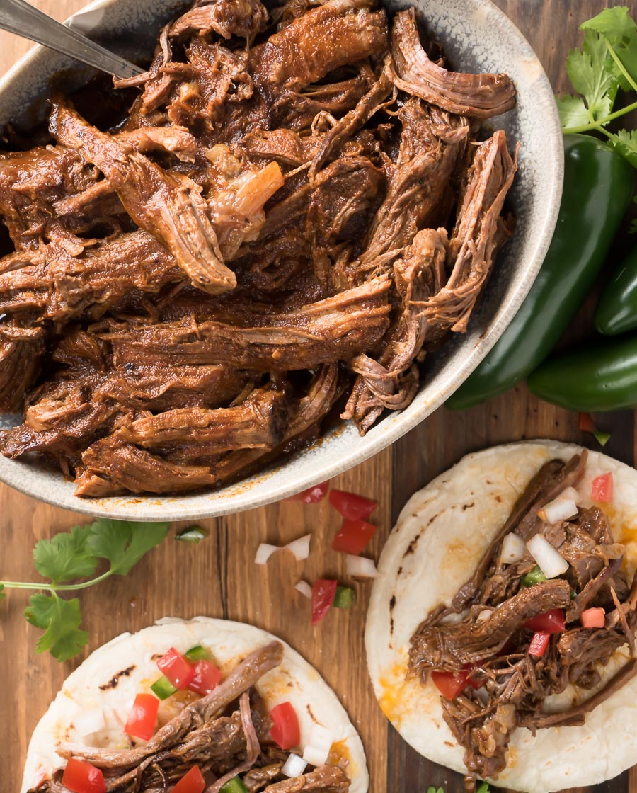 Bowl of beef barbacoa with dressed tacos.