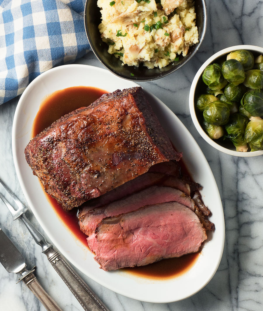 Perfectly medium rare roast beef with demi-glace sauce on oval platter from above.