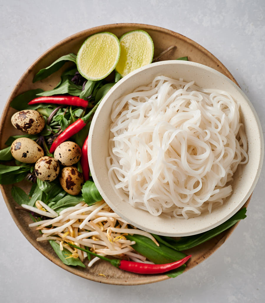 Top shot of rice noodles, red chilies, herbs, quail eggs, limes and bean sprouts.