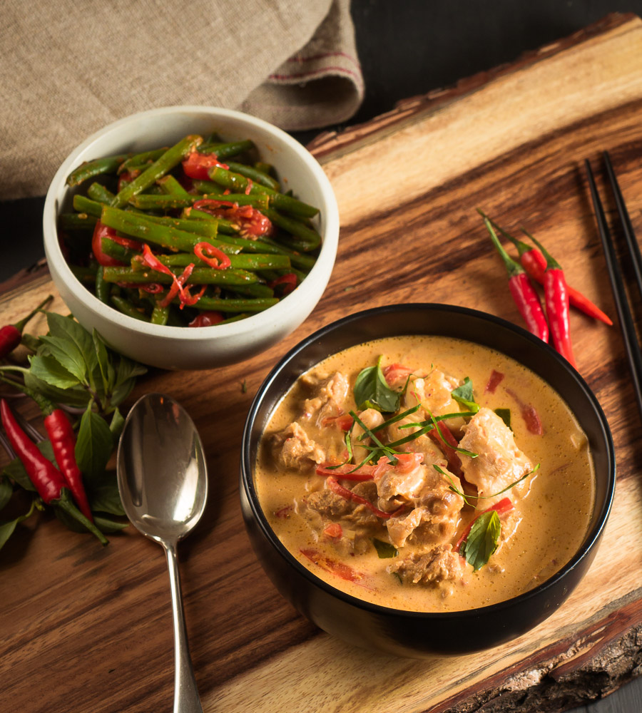 thai red chicken curry in a black bowl with chilies and thai basil