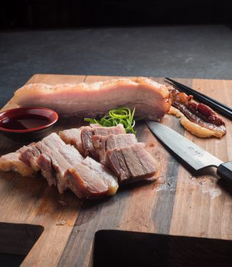 Momofuku pork belly sliced on cutting board with knife and chopsticks