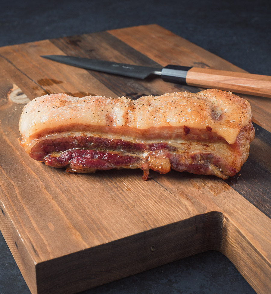 Momofuku pork belly sliced on cutting board with knife and chopsticks