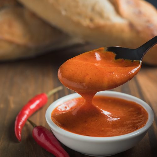 Gochujang mayonnaise in a white bowl with dripping spoon.