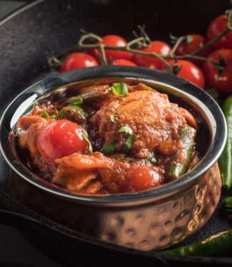 Nearly restaurant chicken jalfrezi in an Indian copper bowl - front view.