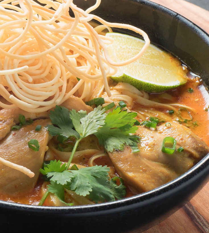 khao soi with fried noodles in a black bowl from the front.