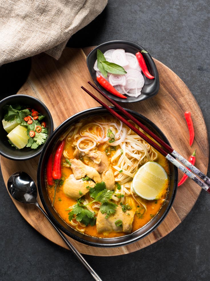 Khao soi in a black bowl surrounded by garnishes - from above.