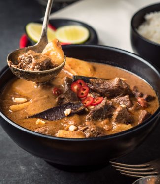 Beef massaman curry in black bowl with ladle.