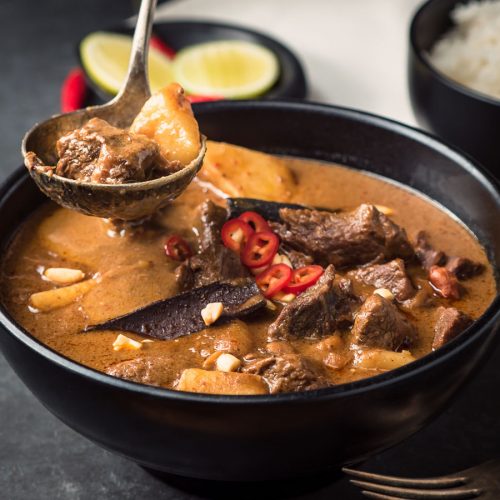 Beef massaman curry in black bowl with ladle.