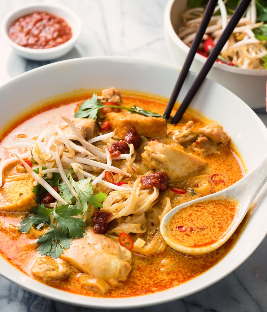 Laksa coconut curry soup in a white bowl from the front. Spoon full of soup in the foreground.