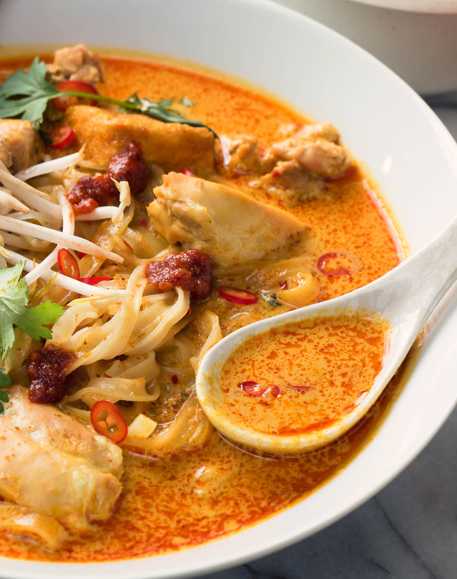 Spoon full of laksa over a bowl of coconut curry soup.