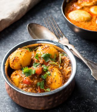 Bombay potatoes in a copper Indian bowl with spoon and fork.