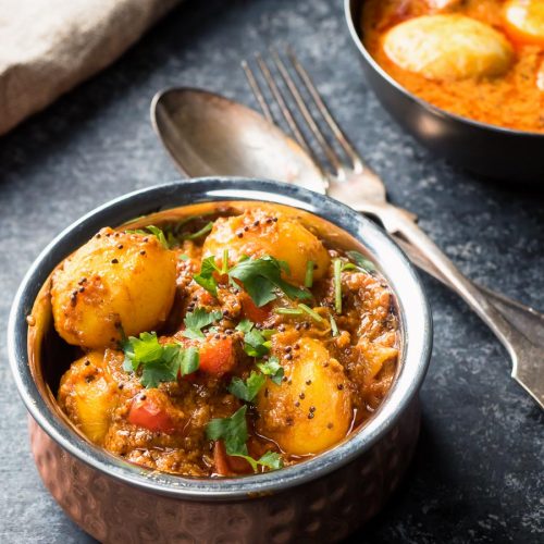 Bombay potatoes in a copper Indian bowl with spoon and fork.