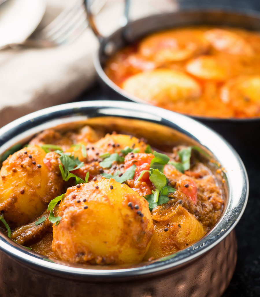 Bombay potatoes close up with egg curry in the background.