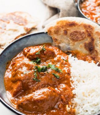 Restaurant butter chicken in a bowl with rice and paratha