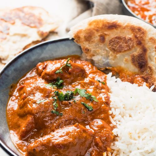 Restaurant butter chicken in a bowl with rice and paratha