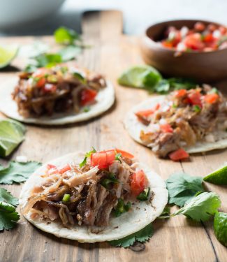 Three carnitas street tacos and bowl of salsa from the front.