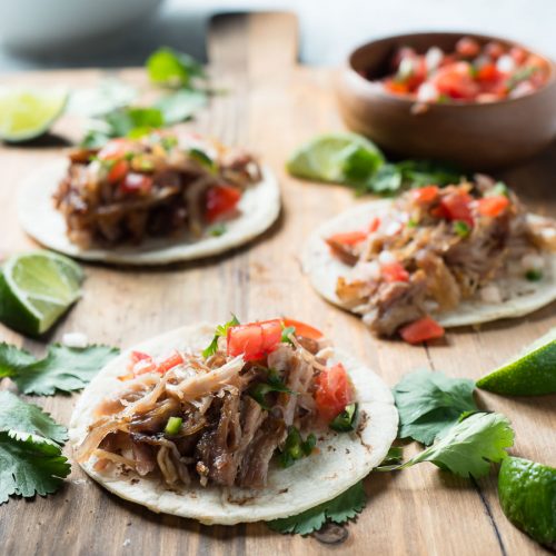 Three carnitas street tacos and bowl of salsa from the front.