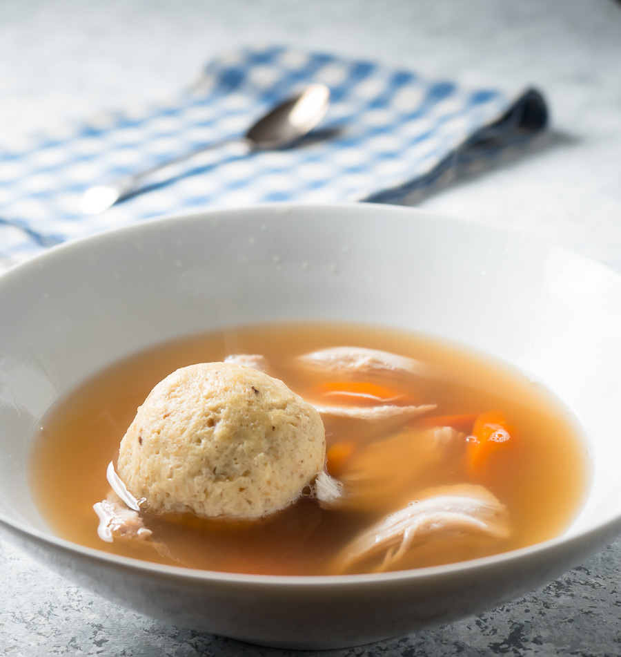 Matzo ball soup in a white bowl from the front.