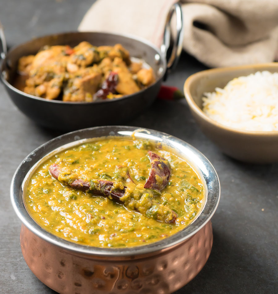 Dal palak in a copper bowl with curries and rice.