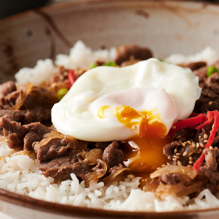 Poached egg on gyudon with yolk dripping into the beef.