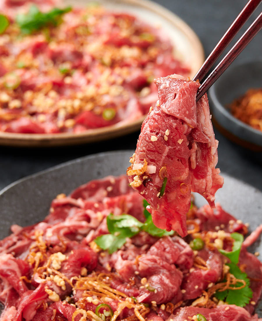 Bite of Asian style carpaccio held with chopsticks.