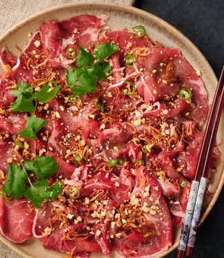 Platter of Asian style carpaccio garnished with sesame, peanuts, cilantro and green chili slices.