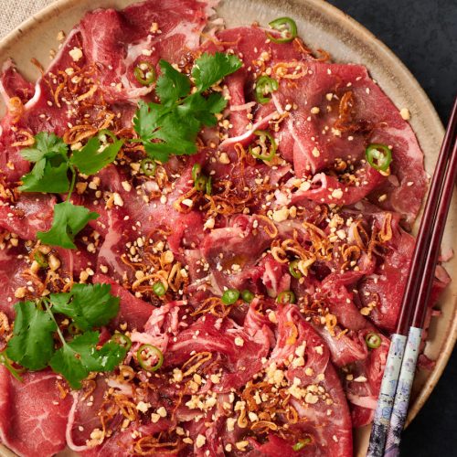 Platter of Asian style carpaccio garnished with sesame, peanuts, cilantro and green chili slices.