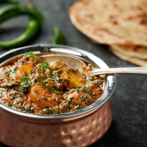 Saag aloo in an Indian copper bowl with spoon.