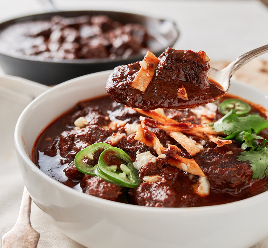 Spoonful of chili colorado above bowl of chili from the front.