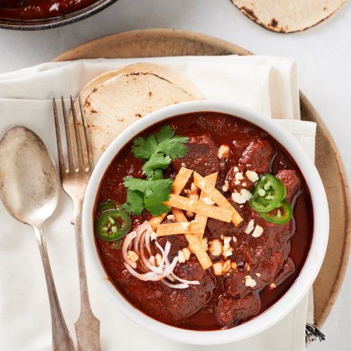 Chili colorado in a white bowl on a large plate from above.