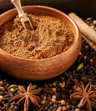 Bowl of garam masala surrounded by whole spices.