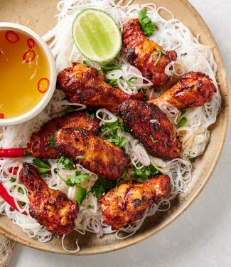 Plate of chicken wings on rice vermicelli with a bowl of nuoc cham from above.