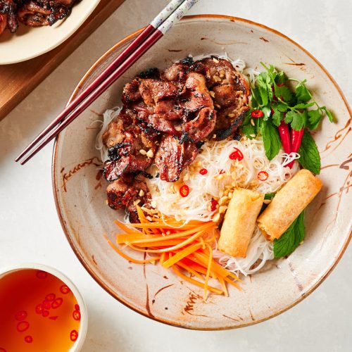 Table scene with grilled pork, pickled carrots, and nuoc cham.