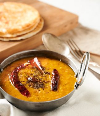 Dal tadka in a bowl with parathas in the background. From the front.