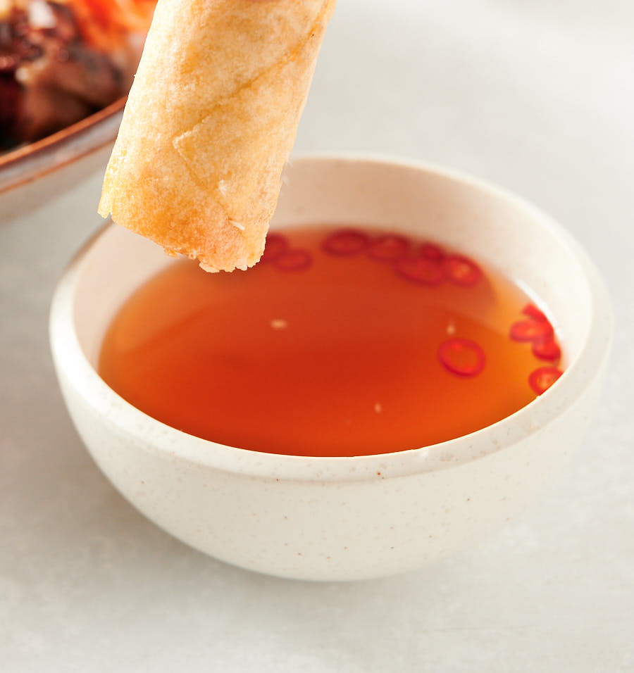 Spring roll held above bowl of nuoc cham.